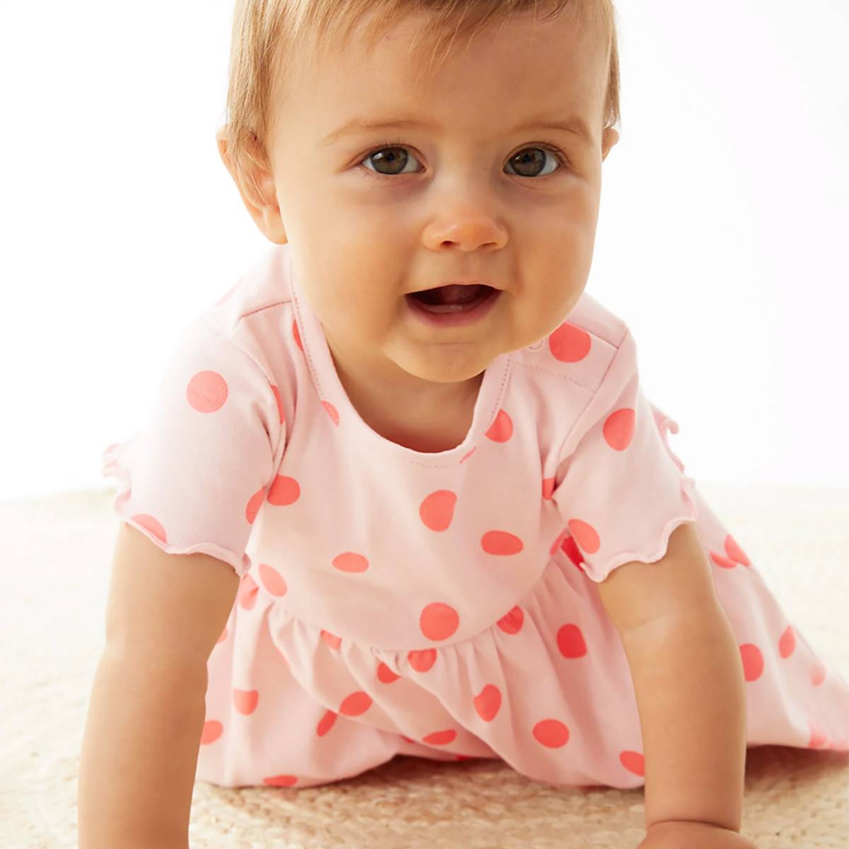 תינוקת לובשת שמלה ורודה עם נקודות. קנו בגדים לתינוקות בנות